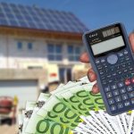 Calculadora sumando dinero frente a vivienda al fondo