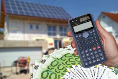 Calculadora sumando dinero frente a vivienda al fondo